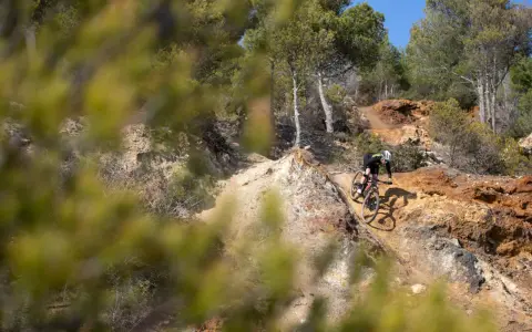Ciclista su un sentiero sterrato, tra rocce e pini, esplora i percorsi MTB Toscana.