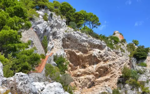 Scogliera rocciosa con una scalinata in mattoni che sale verso la cima, dove si intravede un rudere. Si immagina il **salto di Tiberio** da questo luogo suggestivo.