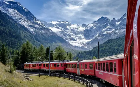 Treni panoramici rossi attraversano un paesaggio alpino mozzafiato con montagne innevate e foreste verdi.