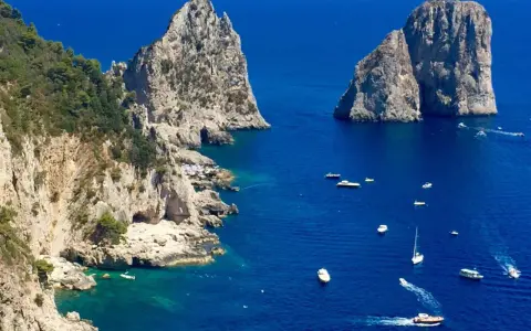 Faraglioni di Capri, tra le più belle isole di Napoli da visitare. Barche navigano nel mare blu intenso.
