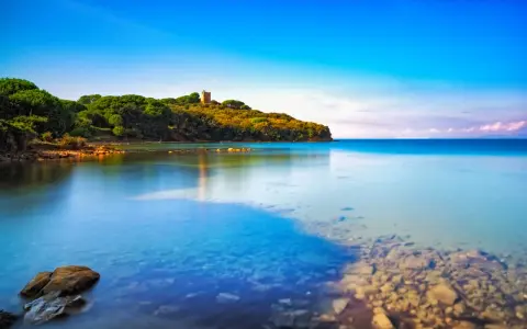 Torre medievale su una collina verdeggiante, con acque cristalline che lambiscono le **punta ala spiagge più belle**.