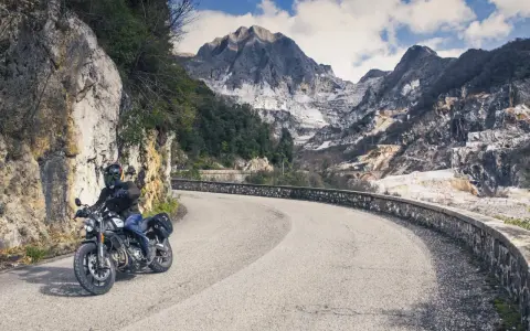 Motociclista su strada tortuosa con montagne di marmo sullo sfondo, un'autentica **Toscana da visitare**.