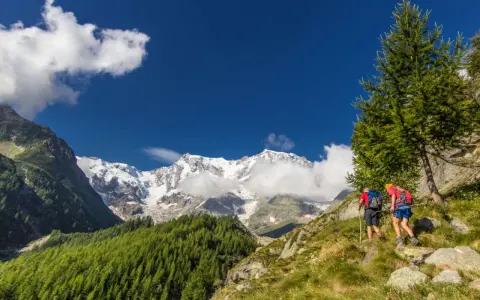 Due escursionisti affrontano un sentiero in Val d'Ossola, con maestose cime innevate sullo sfondo. Perfetto per escursioni facili.