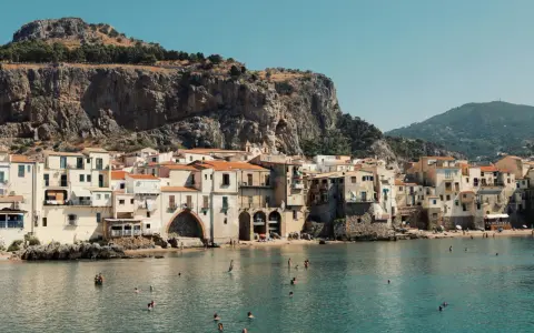 Un incantevole borgo da visitare in Sicilia, con case color pastello affacciate sul mare cristallino e una maestosa roccia a fare da sfondo.