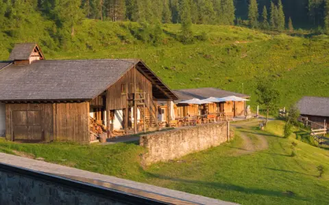 Malghe Alto Adige immerse nel verde, con rustici in legno e tavoli all'aperto sotto ombrelloni bianchi. Un'oasi di pace tra i boschi.