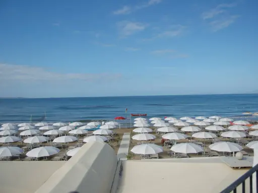 Spiaggia di **Marina di Follonica** con file ordinate di ombrelloni bianchi, mare azzurro e cielo sereno.
