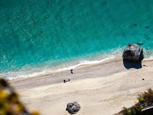 Spiaggia dorata e mare cristallino sulla riviera ligure di ponente. Un pescatore solitario e rocce imponenti.
