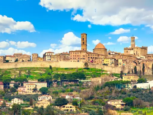 Panoramica di Volterra, dove si trova questo antico borgo toscano, con le sue torri e case arroccate sulla collina sotto un cielo azzurro con nuvole bianche.
