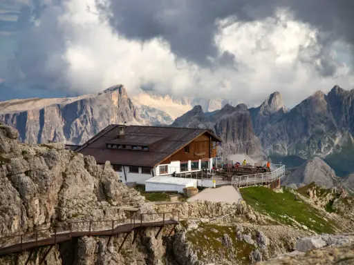 Rifugio alpino con terrazza panoramica, uno dei migliori rifugi dove dormire Dolomiti, incastonato tra imponenti vette rocciose e nuvole minacciose.
