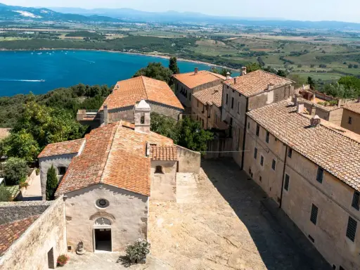 Vista dall'alto del populonia centro storico, con case dai tetti rossi e il mare blu sullo sfondo.