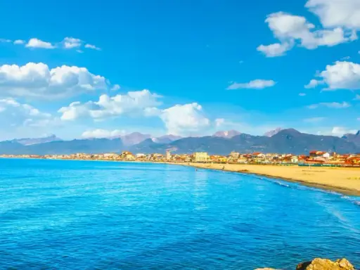 Spiaggia dorata e mare azzurro a Viareggio, con montagne sullo sfondo. Perfetto per scoprire cosa vedere a Viareggio in un giorno.