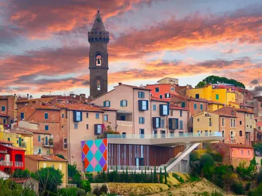 Un borgo italiano con case colorate e una torre campanaria, sotto un cielo infuocato. Potrebbe essere qual è il borgo più bello d'Italia.