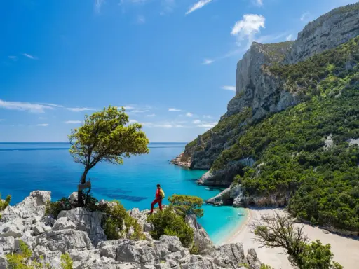 Escursionista ammira una baia cristallina con una spiaggia bianca, incastonata tra imponenti scogliere verdi. Un paesaggio mozzafiato che ricorda la bellezza della montagna centro Italia.