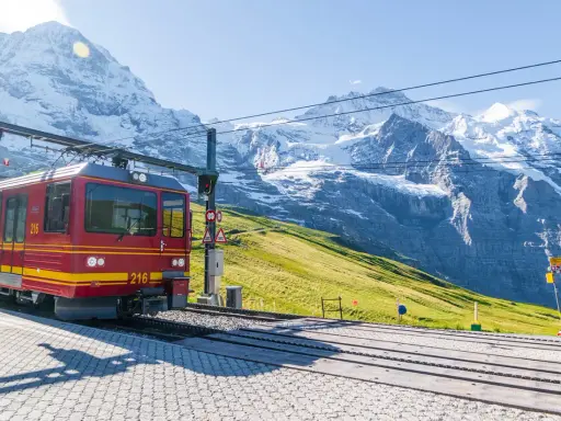 Treno rosso e giallo in stazione, con imponenti montagne innevate sullo sfondo. Un viaggio in treno tra le vette.