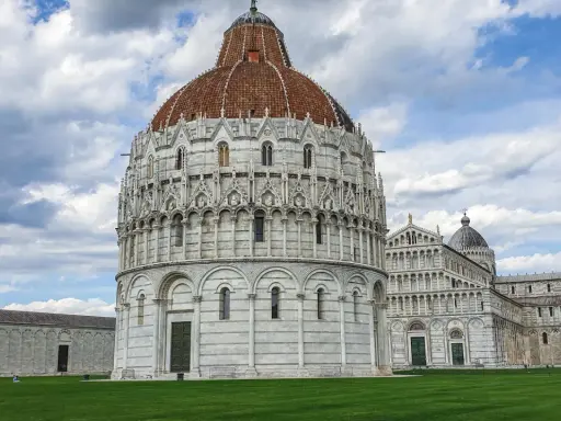 Il Battistero, il Duomo e la Torre Pendente: ecco cosa vedere a Pisa in un giorno, un'iconica piazza con un prato verde e cielo nuvoloso.