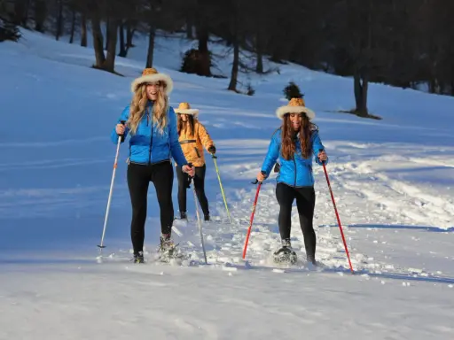 Tre amiche si godono escursioni invernali nelle Dolomiti Bellunesi, camminando sulla neve con le ciaspole e bastoncini.