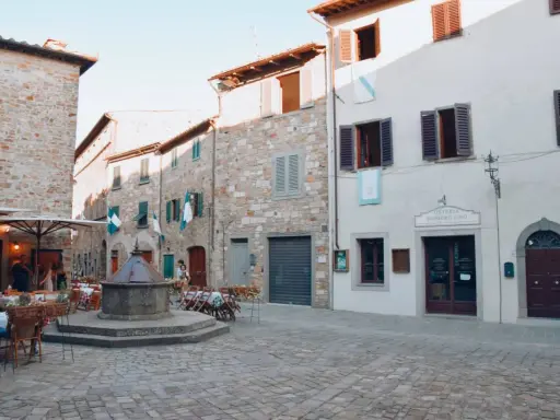 Piazza di San Donato in Poggio con pozzo antico, tavoli all'aperto e l'insegna "Osteria Numero Uno".