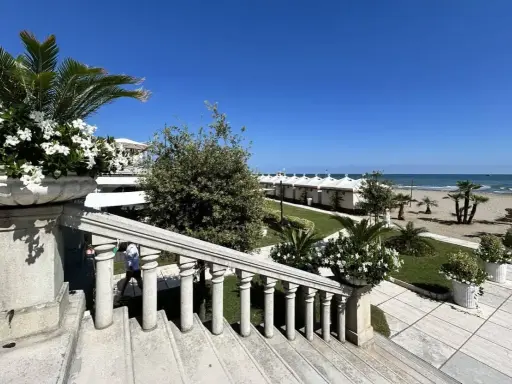 Scalinata in pietra con vasi fioriti, vista su una spiaggia ordinata con cabine bianche, tipica di una città di mare veneto.