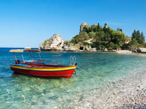 Barca rossa e gialla in acque cristalline, con isolotto verdeggiante sullo sfondo. Un angolo di paradiso che ricorda la bellezza di Sicilia e Sardegna.