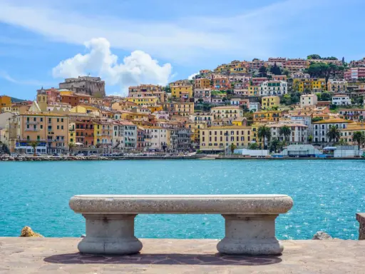Panoramica di Porto Santo Stefano con case colorate a picco sul mare turchese. Un invito a scoprire cosa vedere a Porto Santo Stefano.