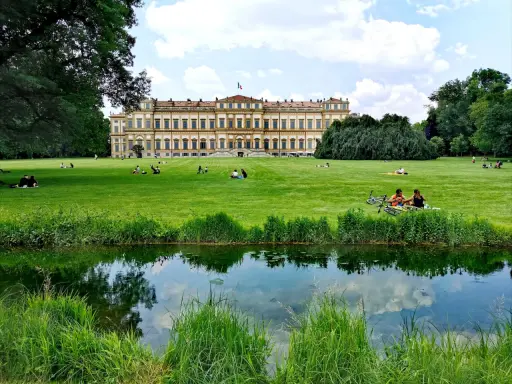 Villa Reale di Monza e il suo parco: un'idea per cosa vedere a Monza in un giorno. Persone rilassate sull'erba, un laghetto e il maestoso edificio.