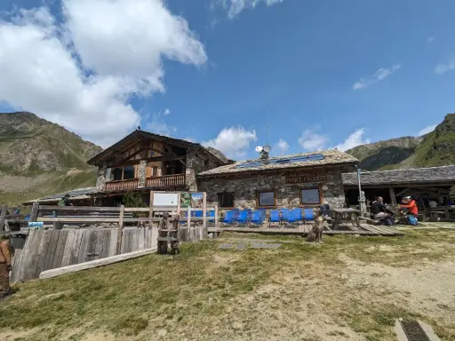 Rifugio Mont Fallère, uno dei rifugi Valle d'Aosta facili, accoglie escursionisti con le sue strutture in pietra e legno, circondato da verdi pendii e montagne.