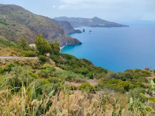 Panoramica mozzafiato per capire come visitare le Isole Eolie: costa verdeggiante, mare blu intenso e isole vulcaniche all'orizzonte.