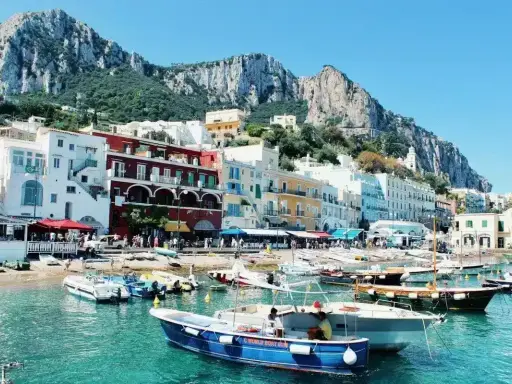 Colorate case affacciate sul mare turchese, con barche ormeggiate e montagne sullo sfondo. Un incantevole scorcio delle isole vicino Napoli.