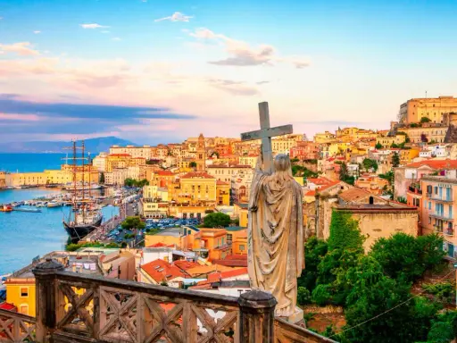 Una statua con una croce domina la vista di una città costiera colorata, perfetta per una gita fuori porta da Roma.