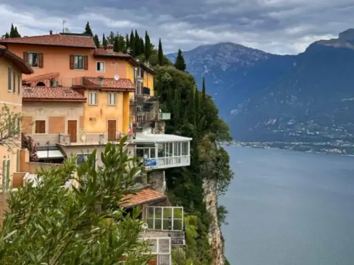 Case colorate aggrappate alla roccia a Tremosine sul Garda, con il lago e le montagne sullo sfondo.