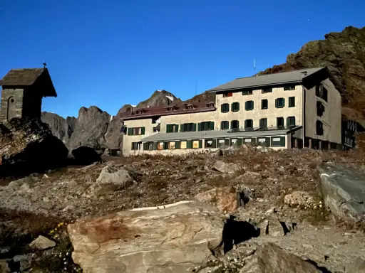 Rifugio alpino con piccola cappella, un esempio di cosa vedere in Lombardia, immerso in un paesaggio roccioso sotto un cielo stellato.