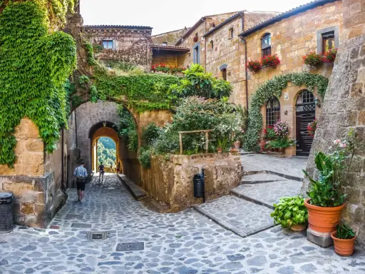 Un vicolo acciottolato tra antichi borghi da visitare nelle Marche, con case in pietra ricoperte di edera e fiori colorati.