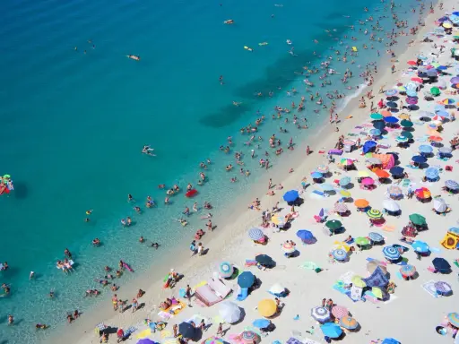 Spiaggia affollata con ombrelloni colorati e bagnanti nell'acqua cristallina, un'immagine perfetta per scoprire le località di mare più economiche in Italia.