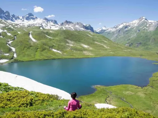 Pace e natura in Valle d'Aosta in estate: un lago alpino azzurro circondato da montagne innevate e verdi pascoli.