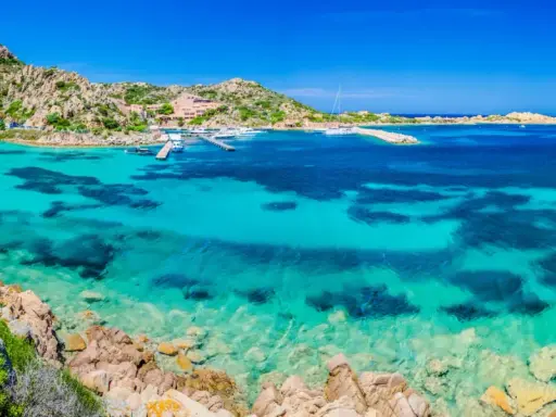Acque cristalline e rocce granitiche ti aspettano per una visita alla Maddalena. Un paradiso azzurro con barche all'ancora.