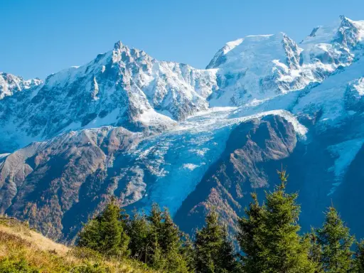 Ghiacciaio imponente tra le montagne italiane più famose, con cime innevate e boschi autunnali.