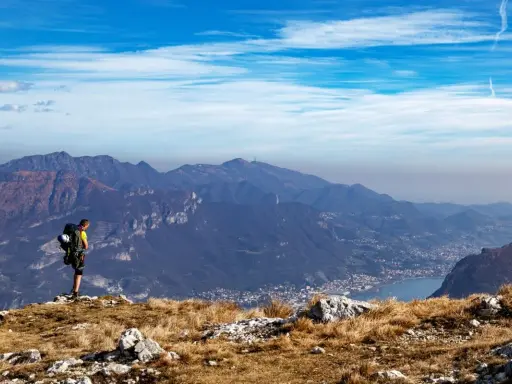 Escursionista ammira la vista panoramica di una montagna vicino Milano, con un lago e un paese in lontananza.