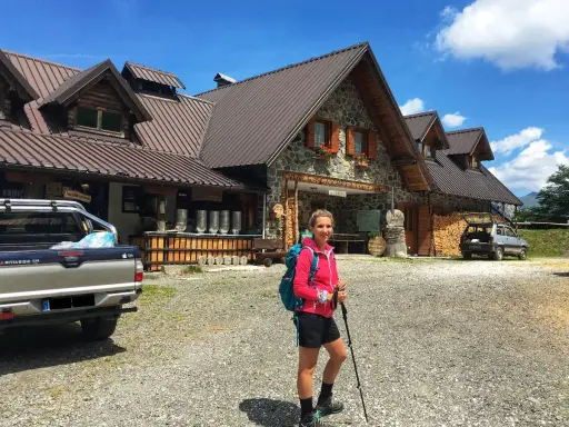 Ragazza con zaino e bastoncini da trekking davanti a un rifugio alpino, una delle tipiche malghe in Friuli.