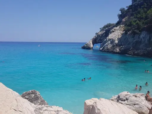 Acqua cristallina e scogliere a picco a Cala Goloritzè, raggiungibile con un suggestivo **percorso a piedi**. Persone nuotano e si rilassano.