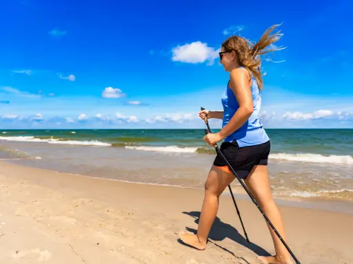 Donna con bastoncini da nordic walking in una splendida passeggiata al mare, con il vento che le scompiglia i capelli.