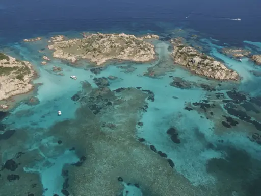 Acque cristalline e isolotti rocciosi, un paradiso dove si trova la Maddalena. Barche navigano in questo mare turchese.