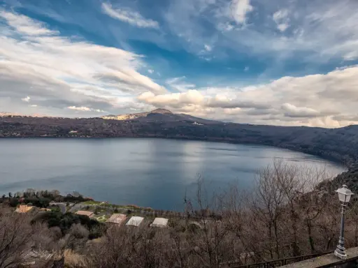 Vista panoramica del lago di Castel Gandolfo, Italia, con colline boscose e un cielo nuvoloso.