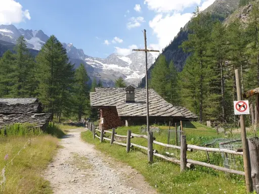 Sentiero di montagna con baite in pietra e tettoie, ideale per cogne escursioni facili. Montagne innevate sullo sfondo.