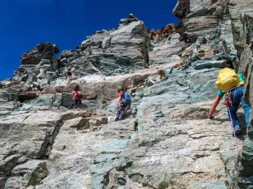 Alpinisti scalano la roccia sul Monviso, seguendo la via normale. Un'avventura sotto il cielo azzurro.