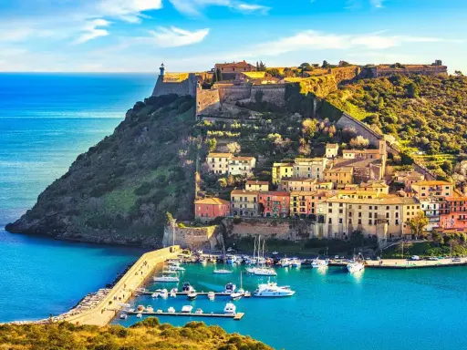Un borgo pittoresco con case colorate aggrappate alla collina, un faro in cima e un porto con barche. Perfetto per andare a zonzo in Toscana.