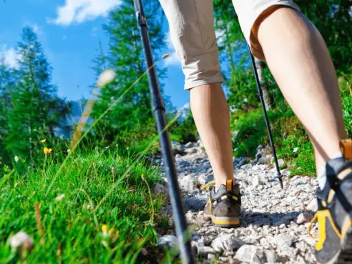 Camminando sul sentiero dei poeti, tra erba verde e fiori gialli, con bastoncini da trekking e scarponi da montagna.