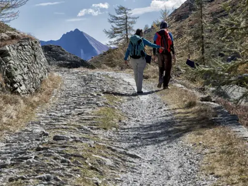 Escursionisti su sentiero sassoso nel Val di Susa, con montagne sullo sfondo.