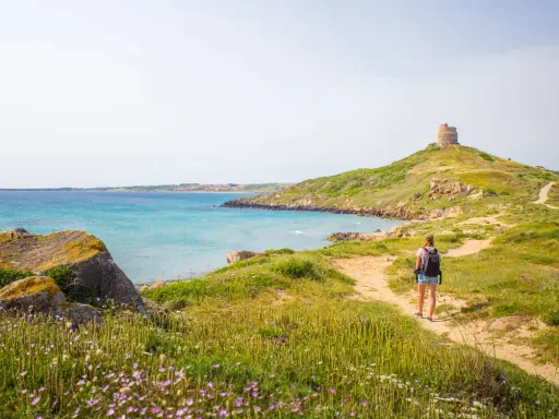 Sentiero panoramico per un tour Sardegna 7 giorni, con torre antica e mare turchese.