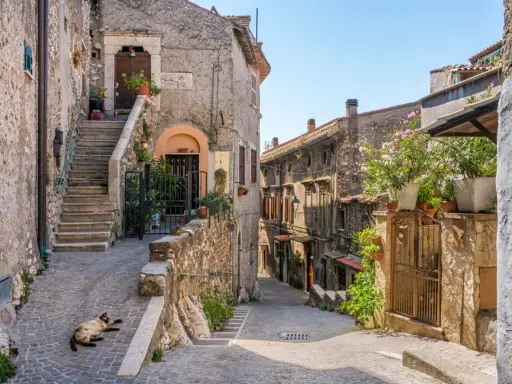 Un gatto si gode il sole in un vicolo acciottolato, tra antiche case di pietra e scale ripide. Un'atmosfera autentica di borghi da visitare nel nord Italia.