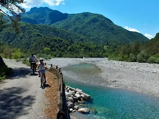 Ciclovia del Tagliamento: due ciclisti esplorano il sentiero panoramico lungo il fiume, circondati da montagne verdi e un cielo azzurro.